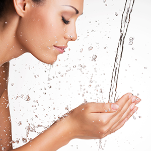 Frau reinigt und erfrischt das Gesicht am Wasserstrahl und zeigt ihre tiefengereinigte Haut.