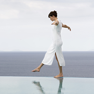 Frau mit schlanker Silhouette zeigt inneres und äusseres Wohlbefinden und hält die Balance auf dem Rand am Pool